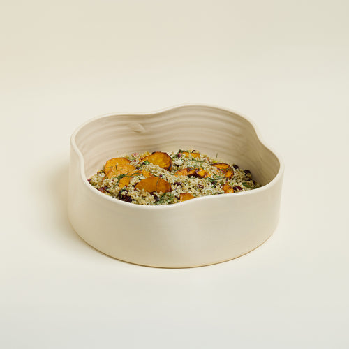 Beige ceramic bowl with a textured surface containing a salad on a light beige background