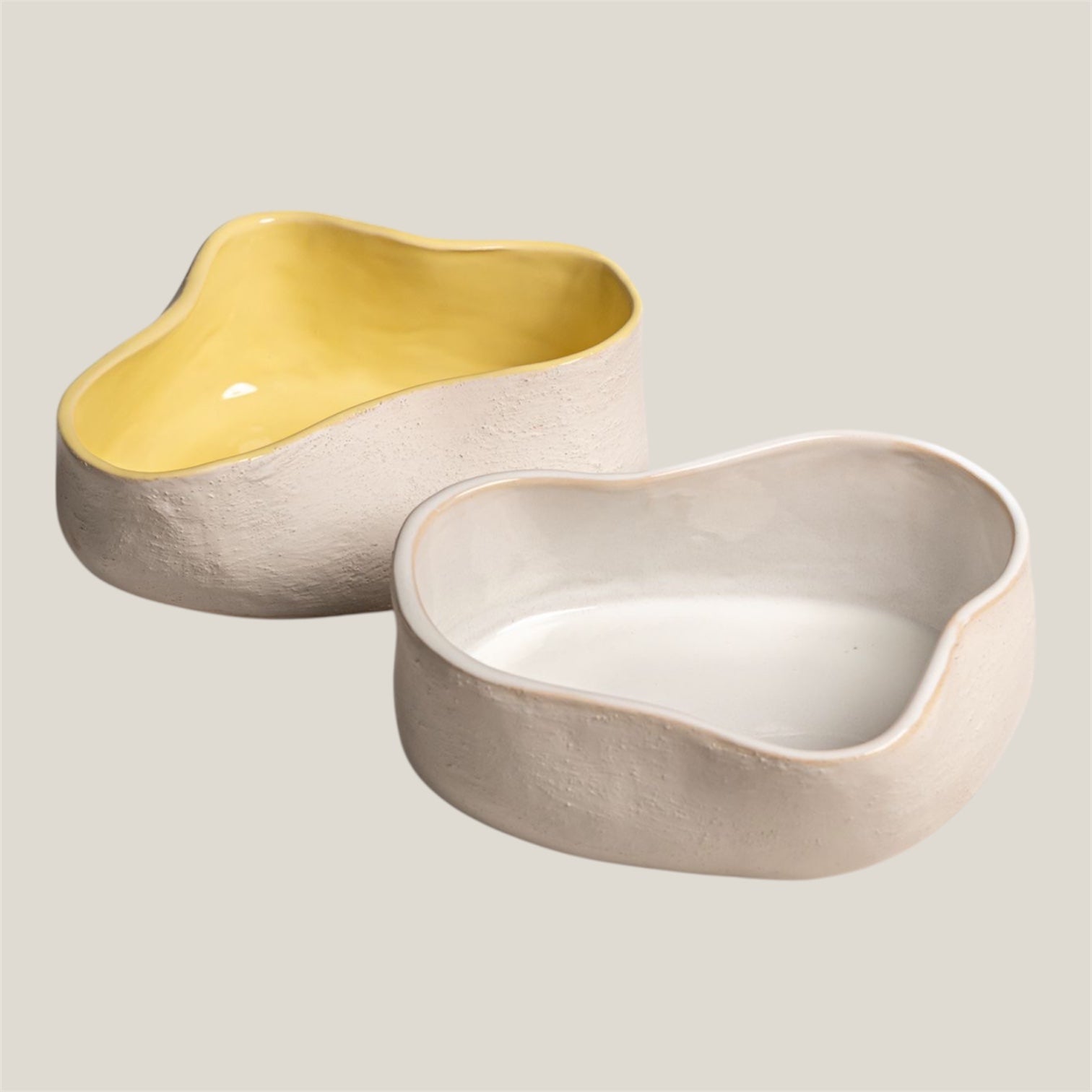 Two ceramic bowls, one yellow and one beige, on a light gray background