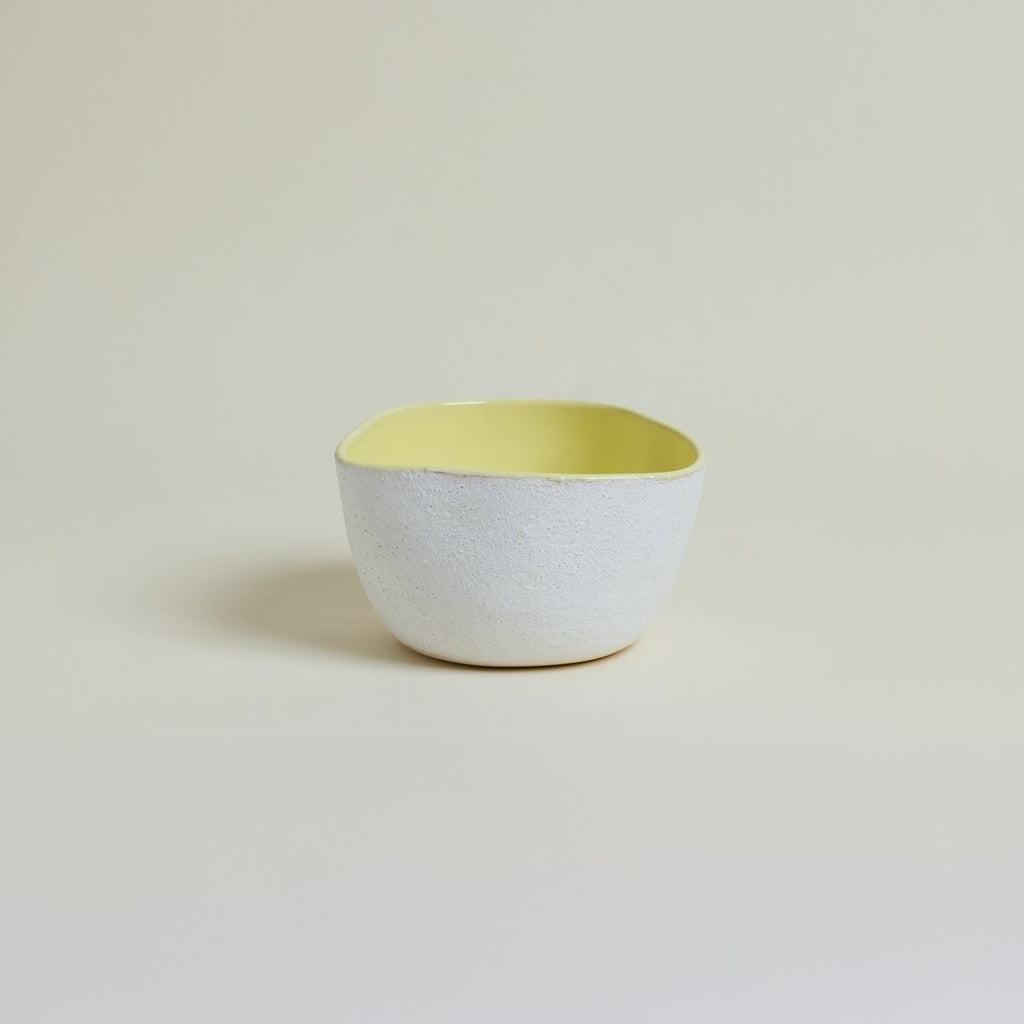Ceramic bowl with a white body and yellow interior on a beige background