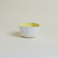 Ceramic bowl with a white body and yellow interior on a beige background