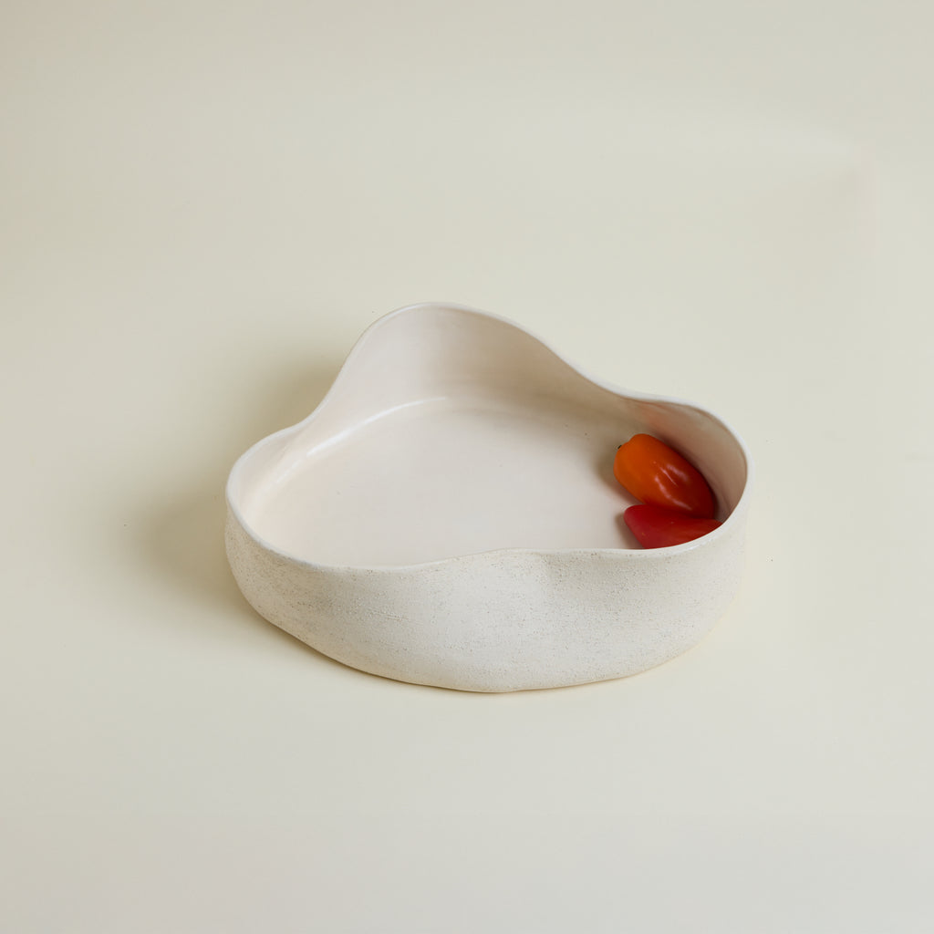 White ceramic dish with a red and orange object inside on a beige background