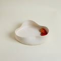 White ceramic dish with a red and orange object inside on a beige background