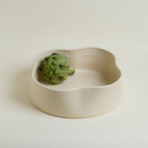 Ceramic bowl with a green artichoke on a beige background